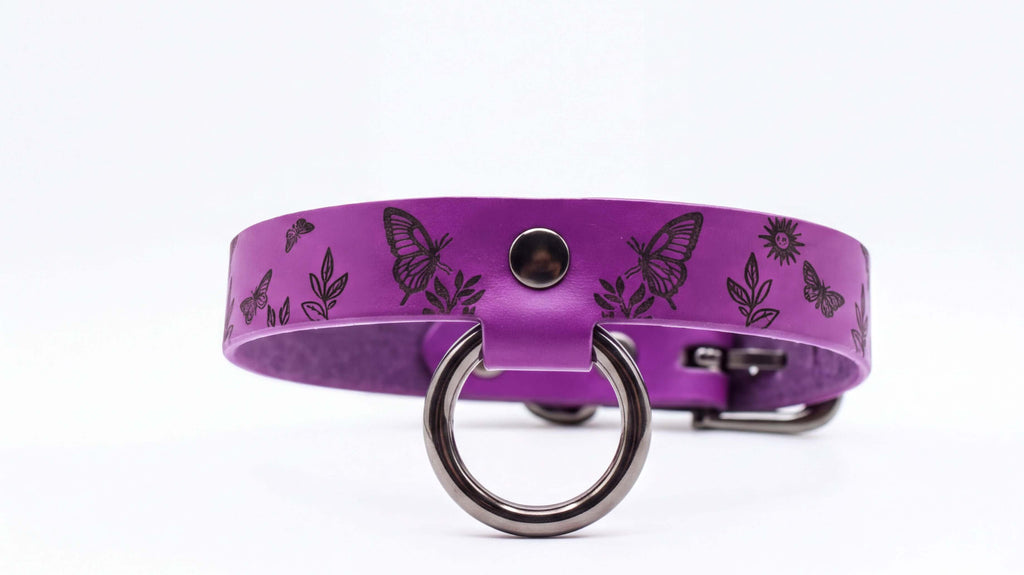 A purple leather collar with a metal ring and butterfly designs.
