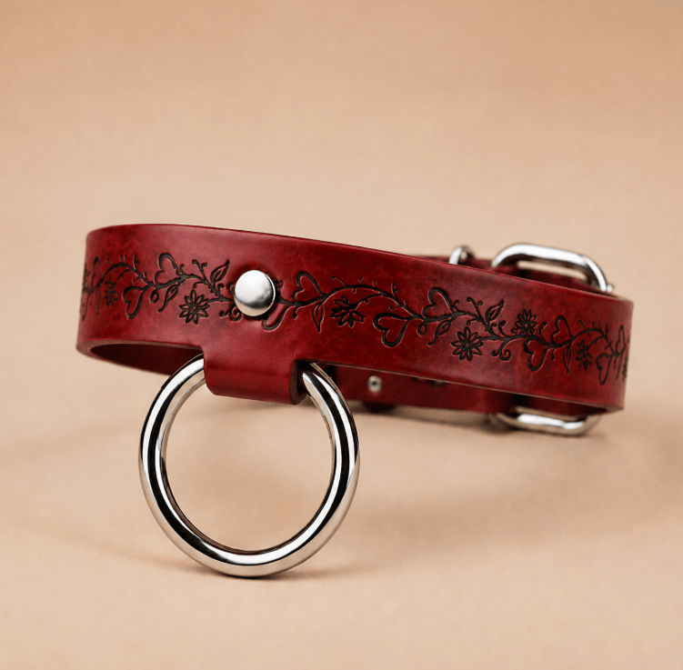 A red leather dog collar with a metal ring and a floral design on the band.