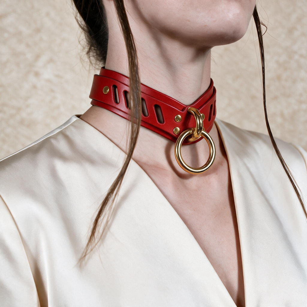 A close-up of a person wearing a red leather choker necklace with a gold ring, against a plain background.
