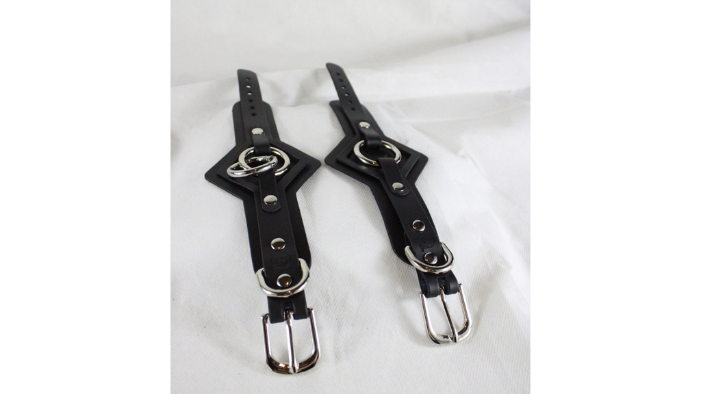 a pair of black leather straps with metal buckles and buckles, placed on a white surface.
