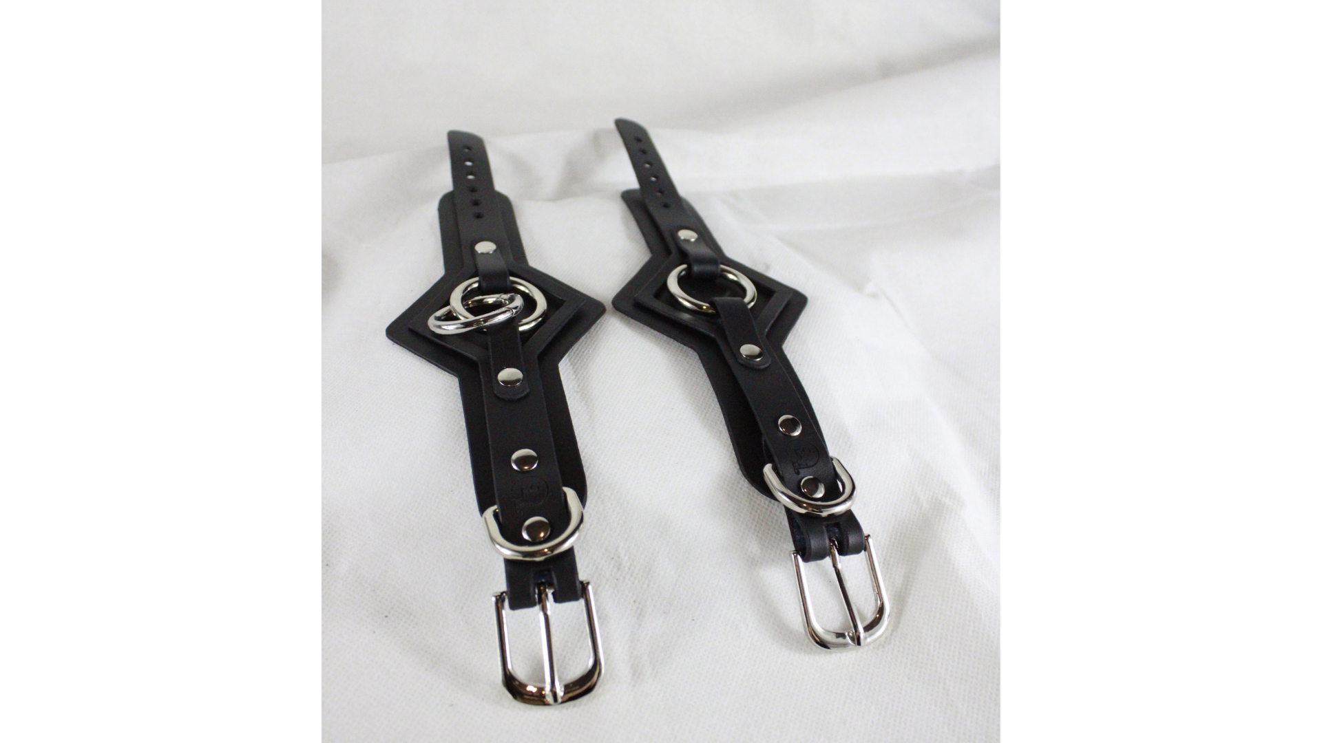 a pair of black leather straps with metal buckles and buckles, placed on a white surface.