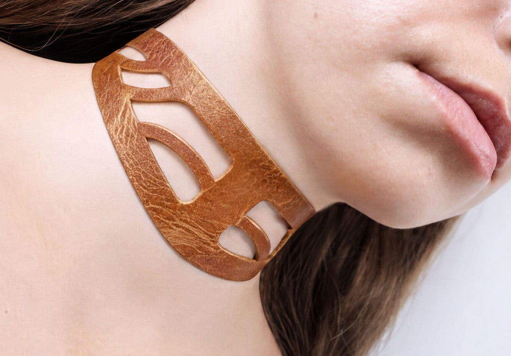 A close-up of a woman's neck and chin wearing a gold-colored choker necklace.