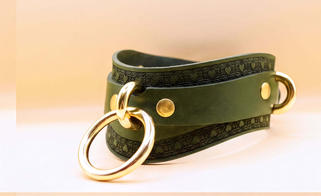 A green leather choker necklace with a gold ring and two gold-colored metal rings on either side.