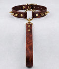 A brown leather choker collar with gold studs and a gold-colored loop, hanging from a gold-colored loop.