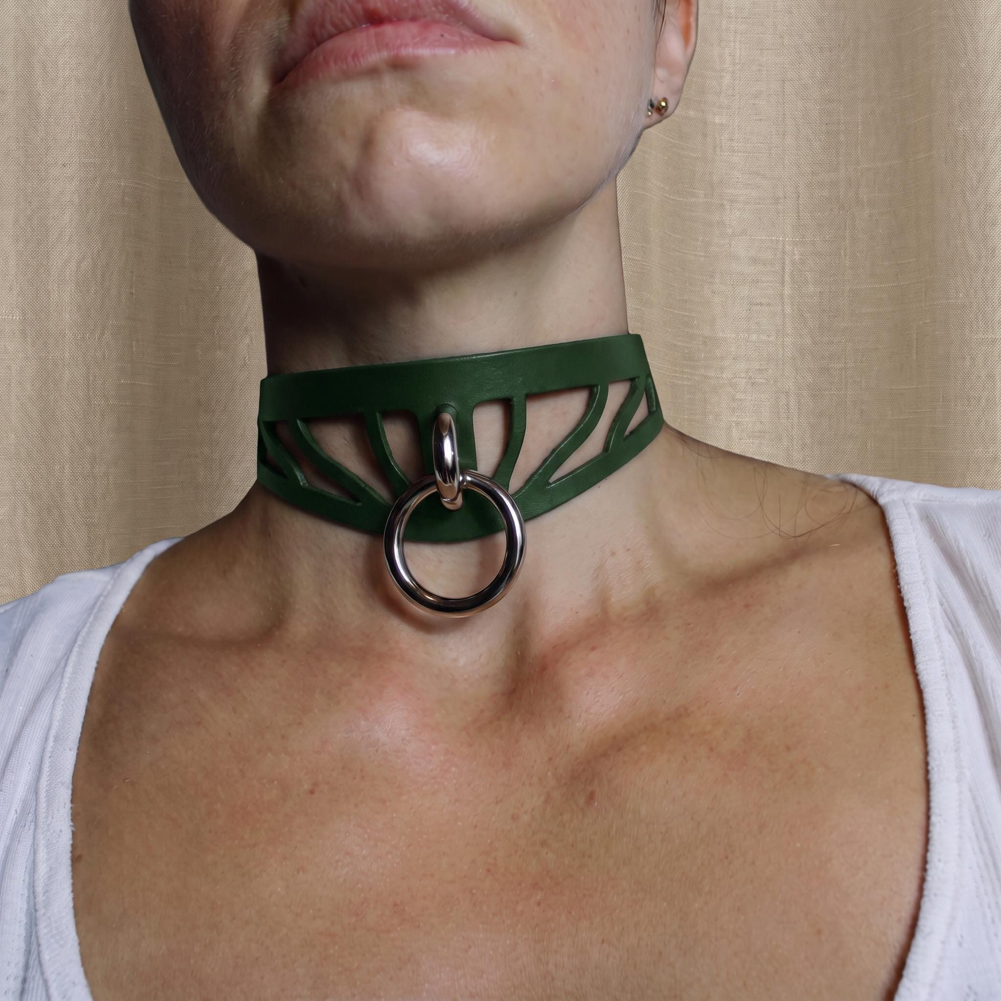 A close-up of a person's neck and chest area wearing a green choker necklace with a metal ring.