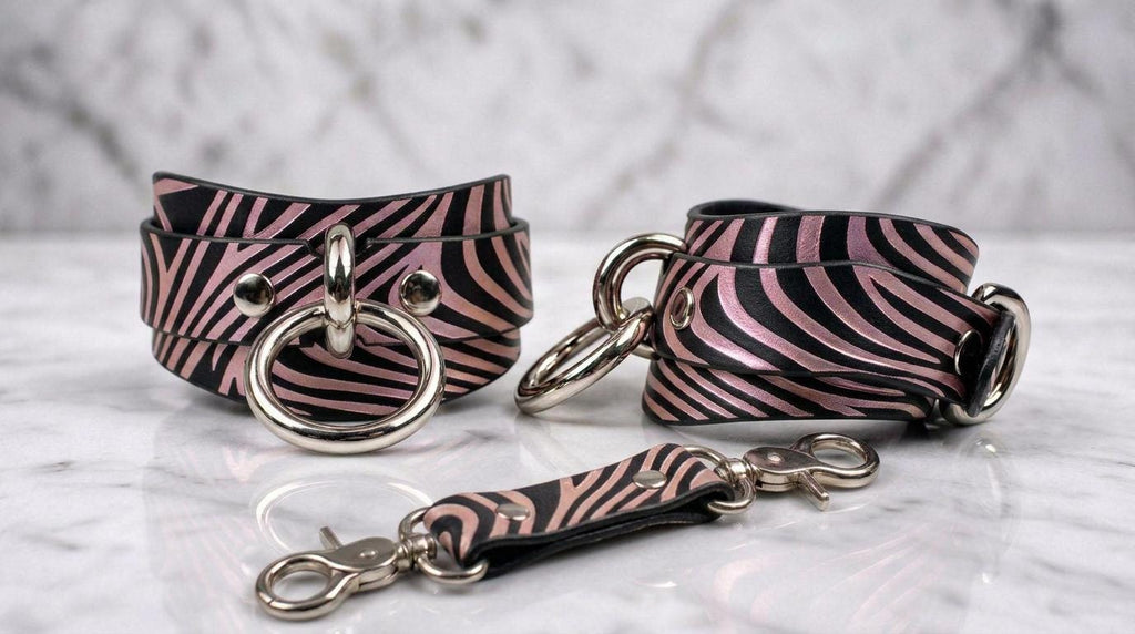 A pair of zebra-striped leather cuffs with metal rings and buckles, displayed on a marble surface.