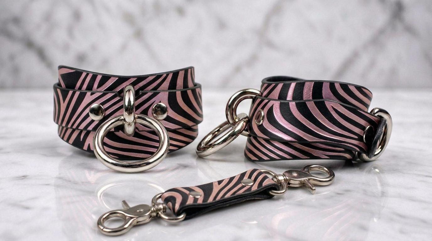 A pair of zebra-striped leather cuffs with metal rings and buckles, displayed on a marble surface.