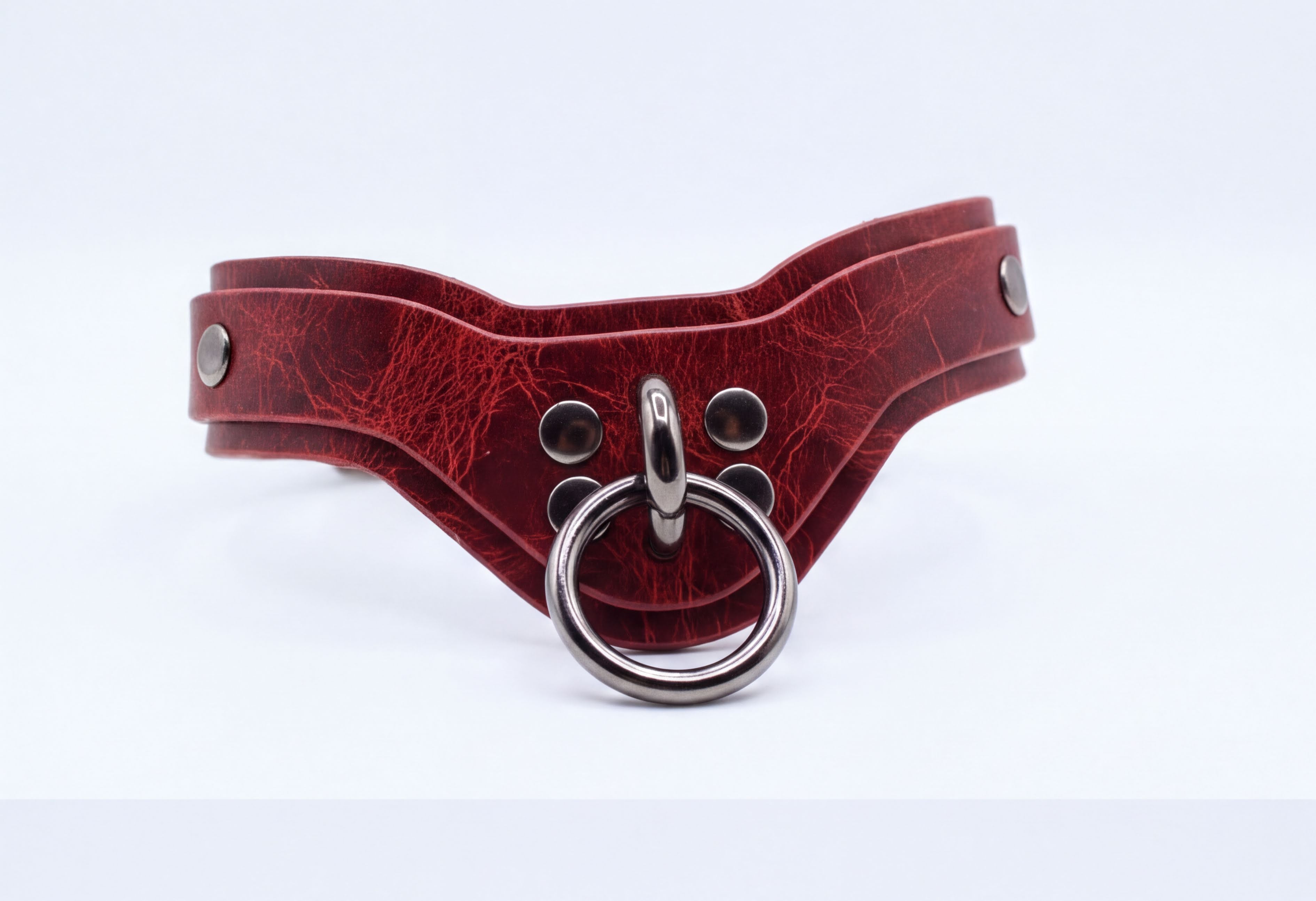 A red leather choker collar with a metal ring and three metal studs on the front.