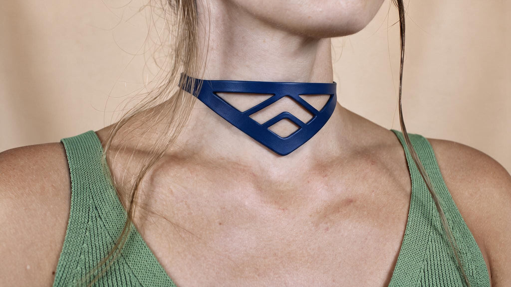 A close-up of a woman's neck and chest area wearing a green sleeveless top and a blue geometric necklace.
