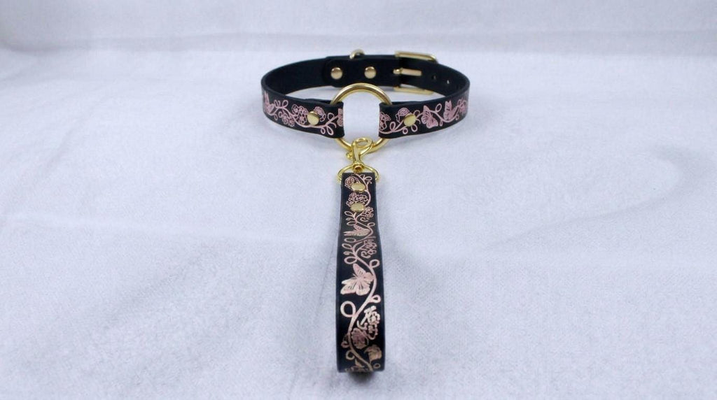 A black leather collar with a gold-colored metal clasp and a floral pattern on the strap.