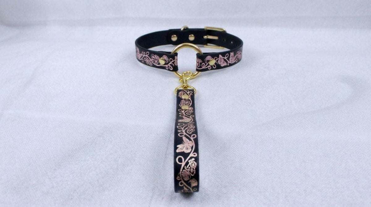 A black leather collar with a gold-colored metal clasp and a floral pattern on the strap.