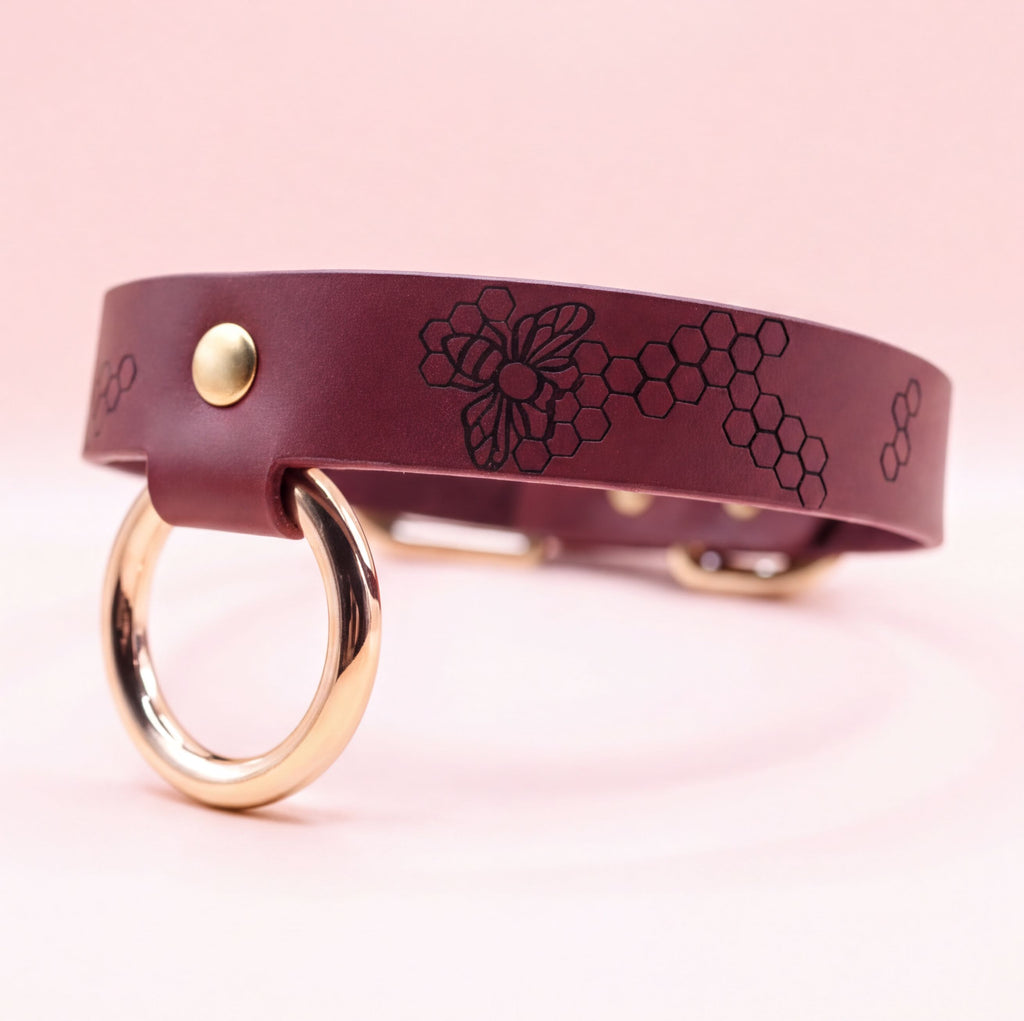 A burgundy leather collar with a gold-colored metal ring and a floral design on the band.