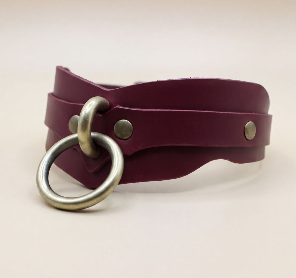 A burgundy leather choker necklace with a metal ring and two metal studs on the collar.