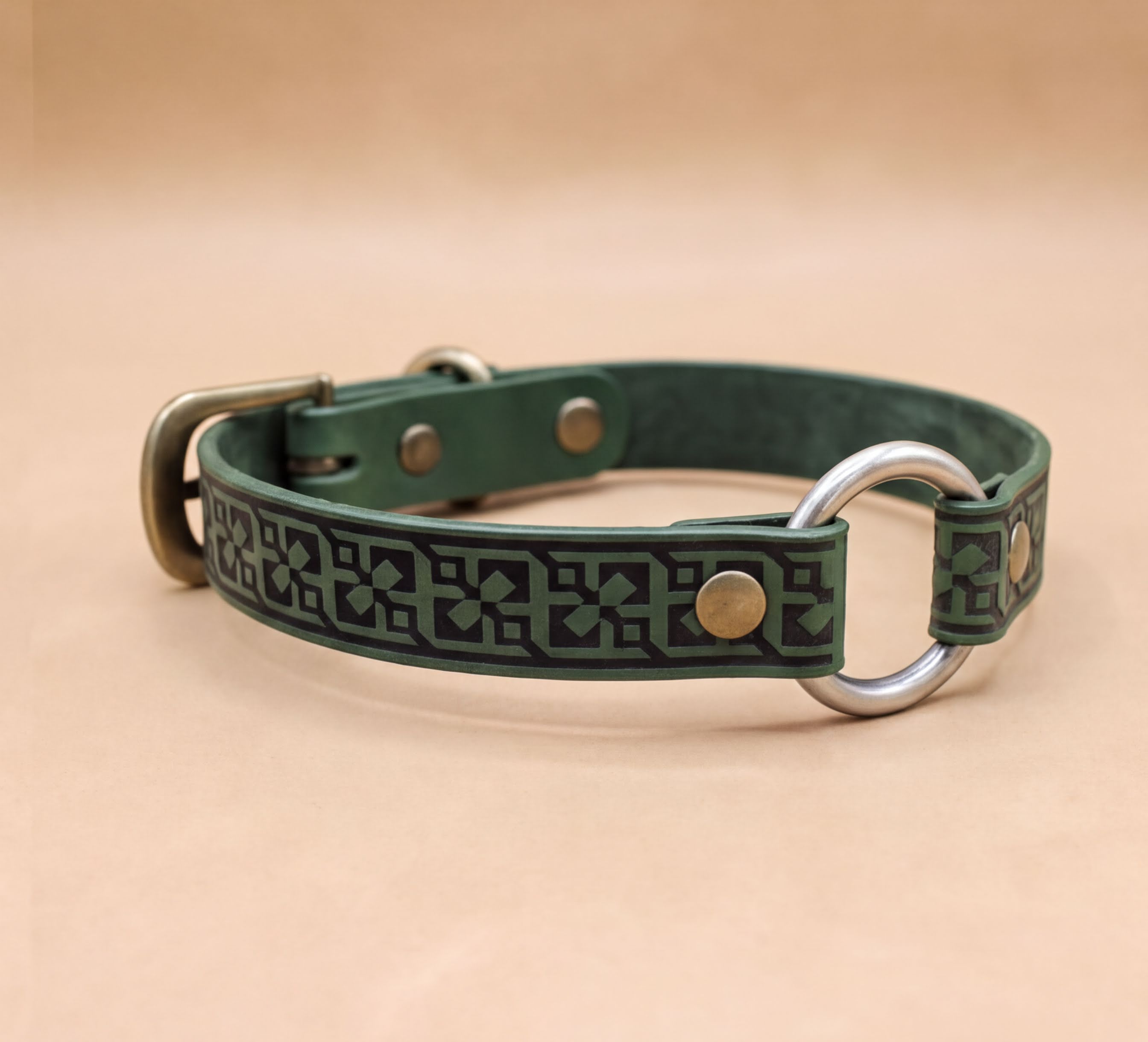 A green leather dog collar with a metal ring and buckle, featuring a decorative pattern on the strap.