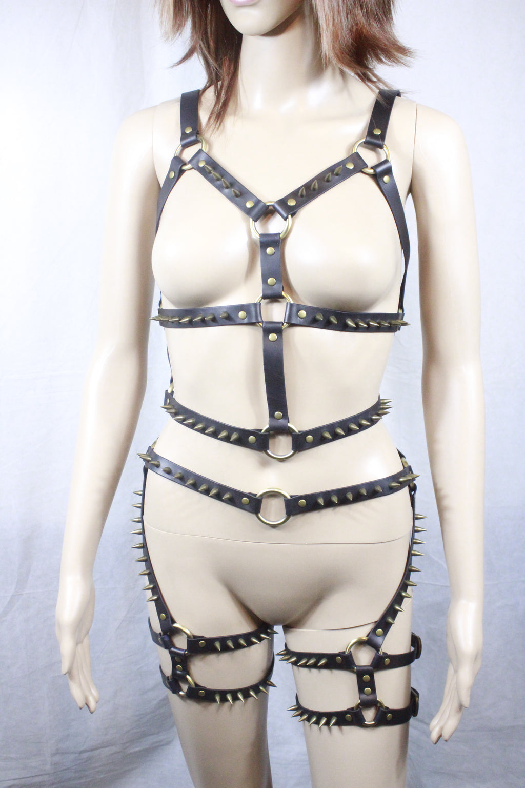 A mannequin wearing a unique and daring outfit consisting of a strapless top with a low-cut neckline, black leather straps with spikes, and a corset-style bra.