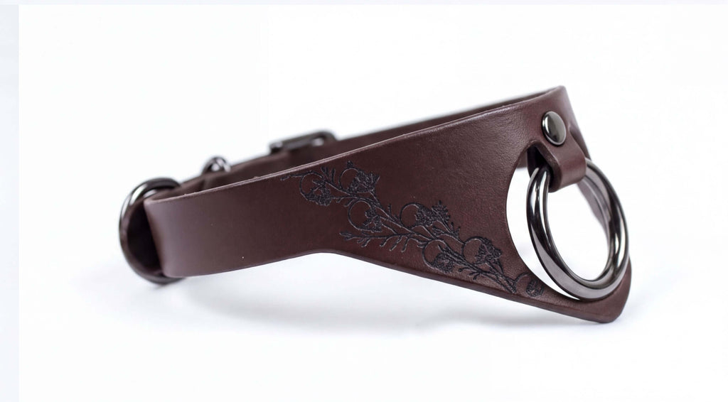 A brown leather collar with a metal ring and a floral design on the side.