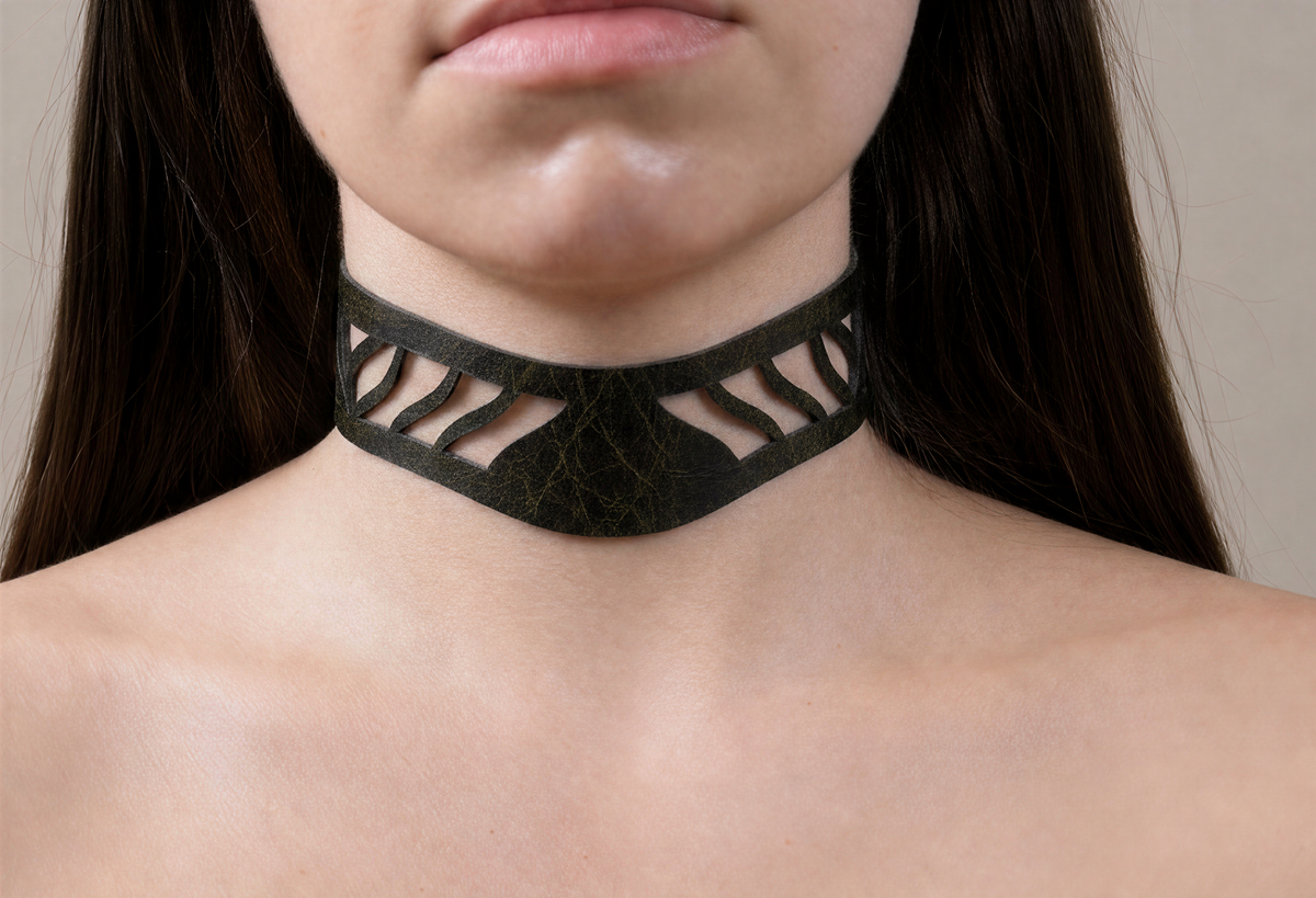 A close-up of a person's neck and chest area, featuring a choker-style necklace with a unique cutout design.