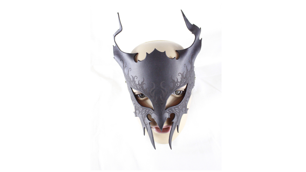 A dark, ornate mask with sharp, pointed features and a fierce expression, resembling a creature or monster.