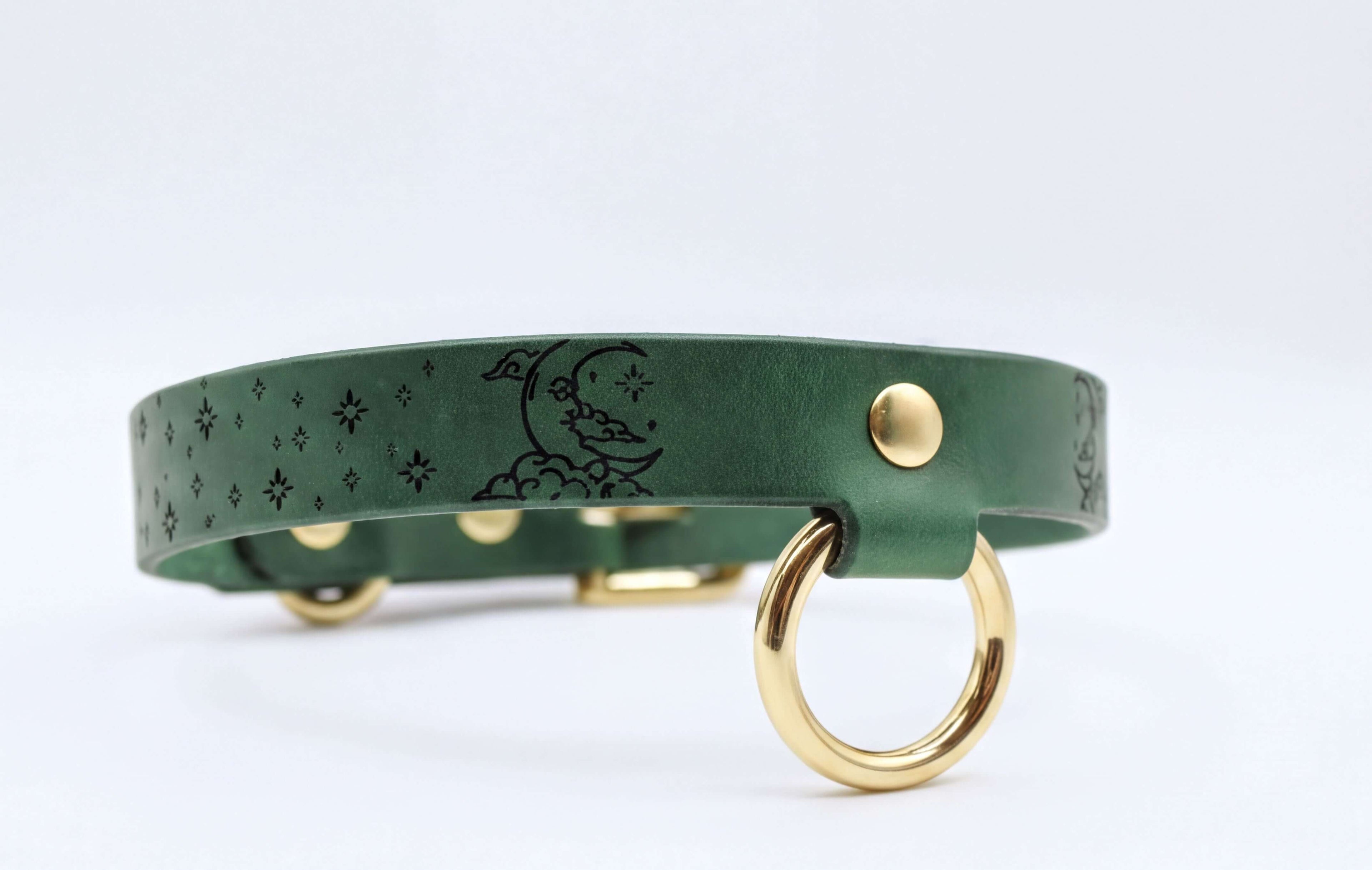 A green leather collar with a moon and star design, featuring a gold-colored metal ring on the front.