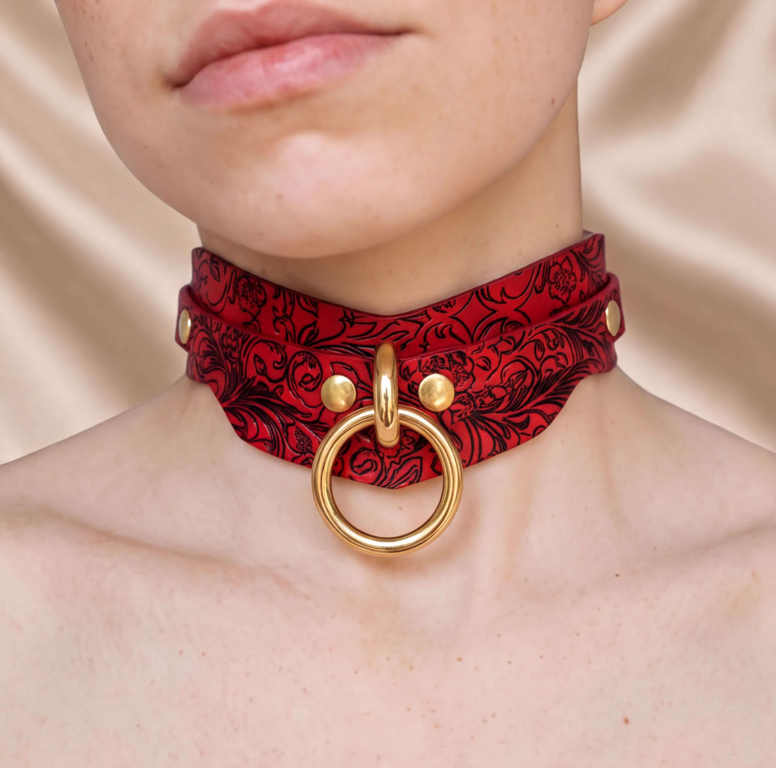 A close-up of a person's neck wearing a red and black choker necklace with a gold ring and buckle.