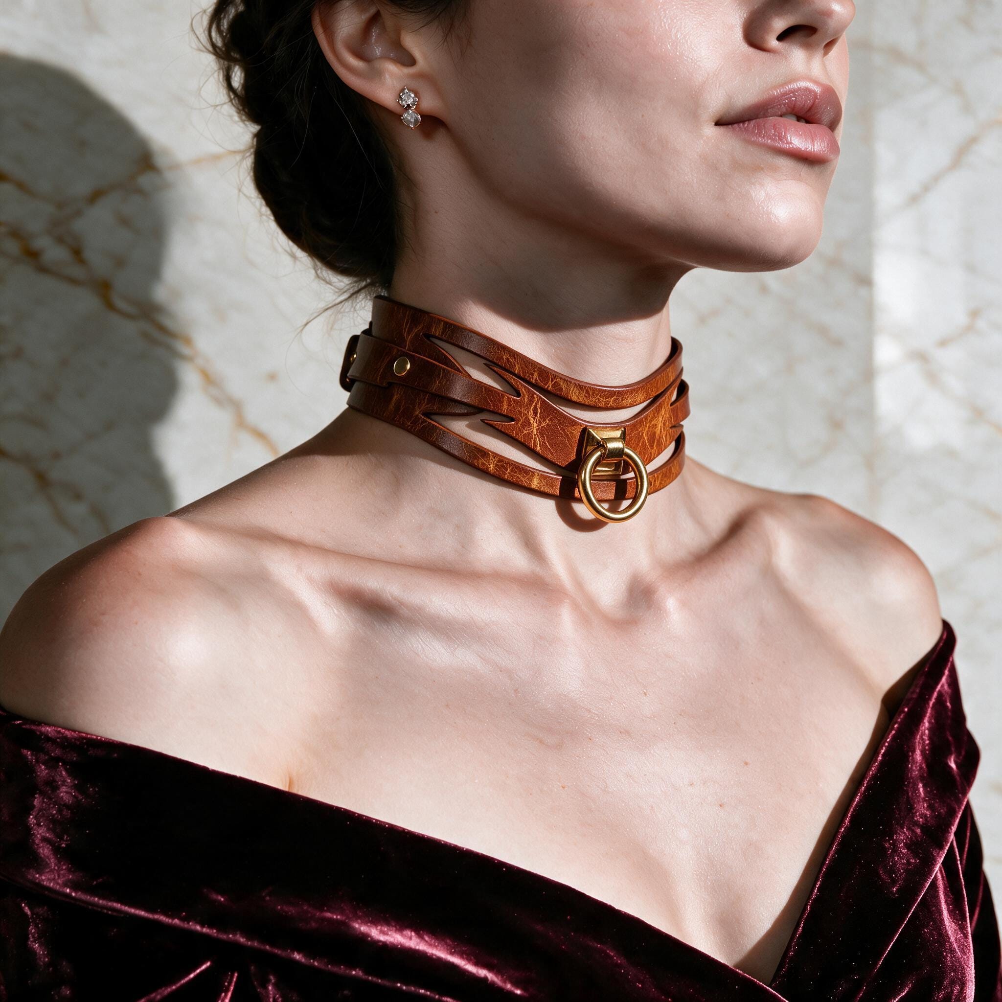 A woman wearing a brown leather choker necklace with a gold buckle, posing against a marble wall.