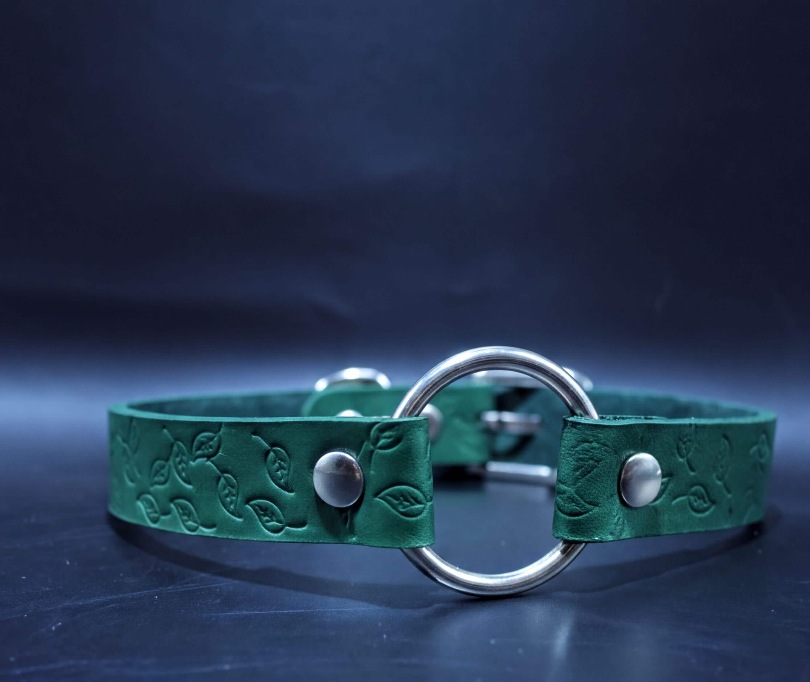 A green leather collar with a metal ring and leaf-shaped embellishments.