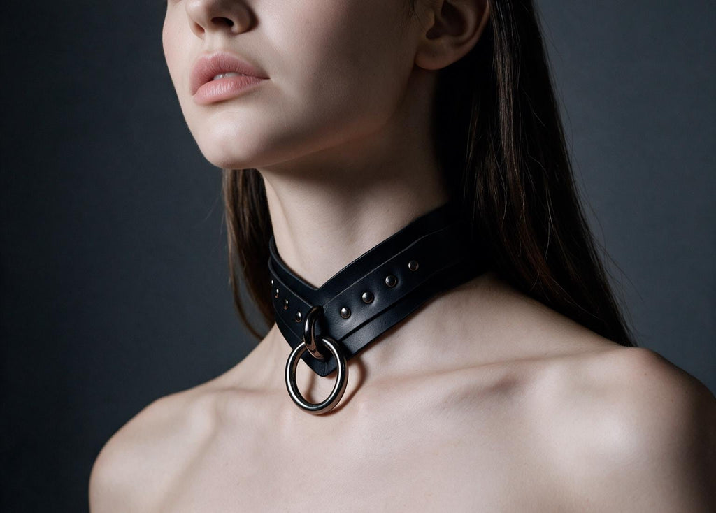 A close-up of a woman's neck and chest area wearing a black leather choker necklace with a metal ring.