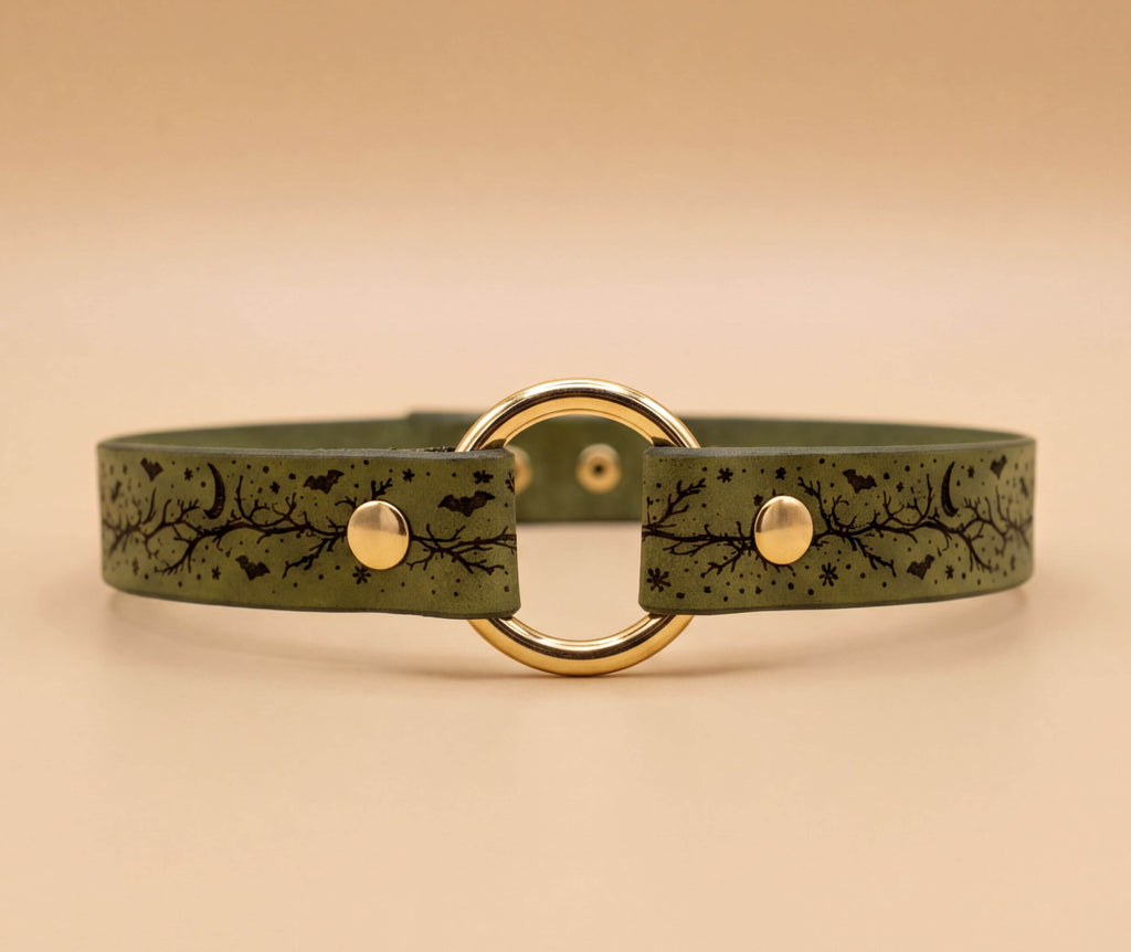 A green leather choker necklace with a gold-colored circular buckle and a leaf-like pattern design.