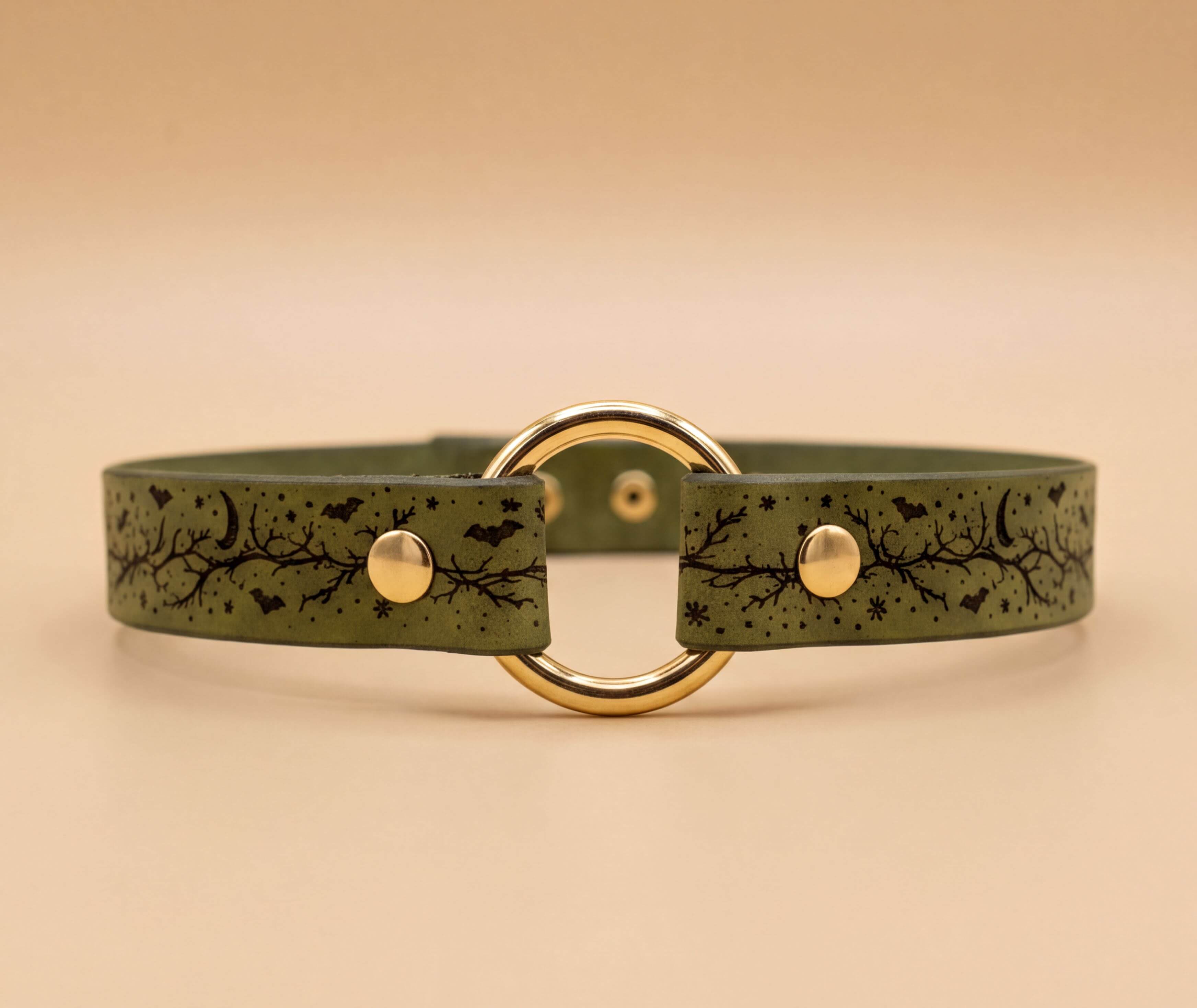 A green leather choker necklace with a gold-colored circular buckle and a leaf-like pattern design.