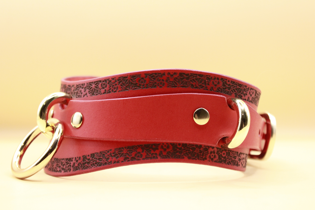 A red leather strap with a floral pattern and two gold-colored buckles.