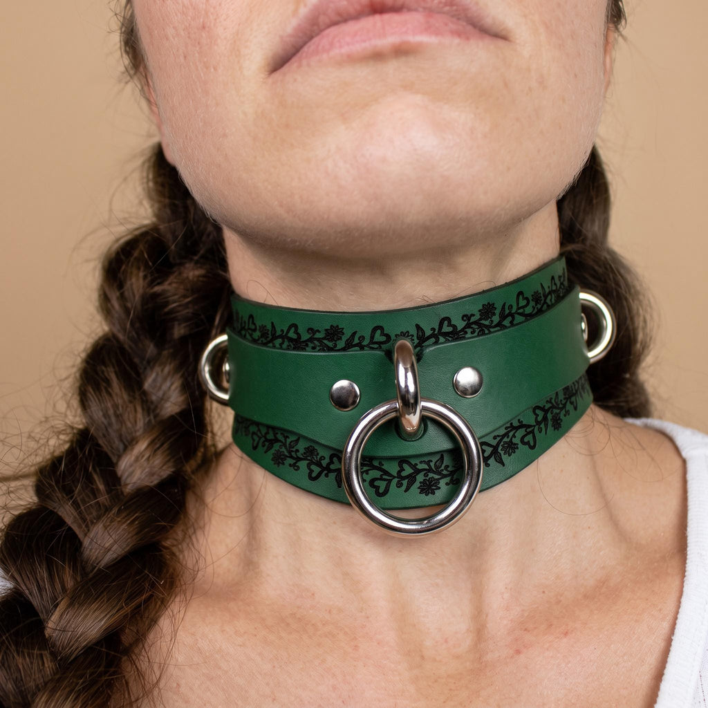 A close-up of a woman's neck wearing a green leather choker necklace with metal rings and a circular metal ring.