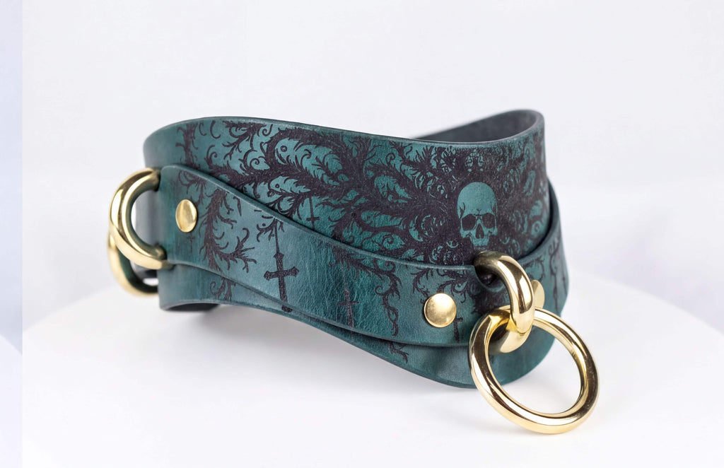 A green leather choker necklace with a skull design and gold-colored metal rings.