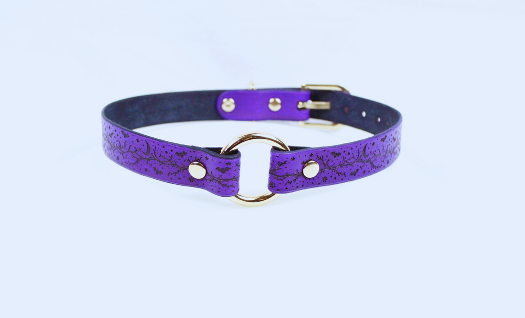 A purple leather choker collar with a gold-colored metal ring and buckle.