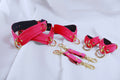 Bondage Gear pink restraint set with collar, cuffs, and connectors for BDSM play, featuring gold hardware and soft leather.