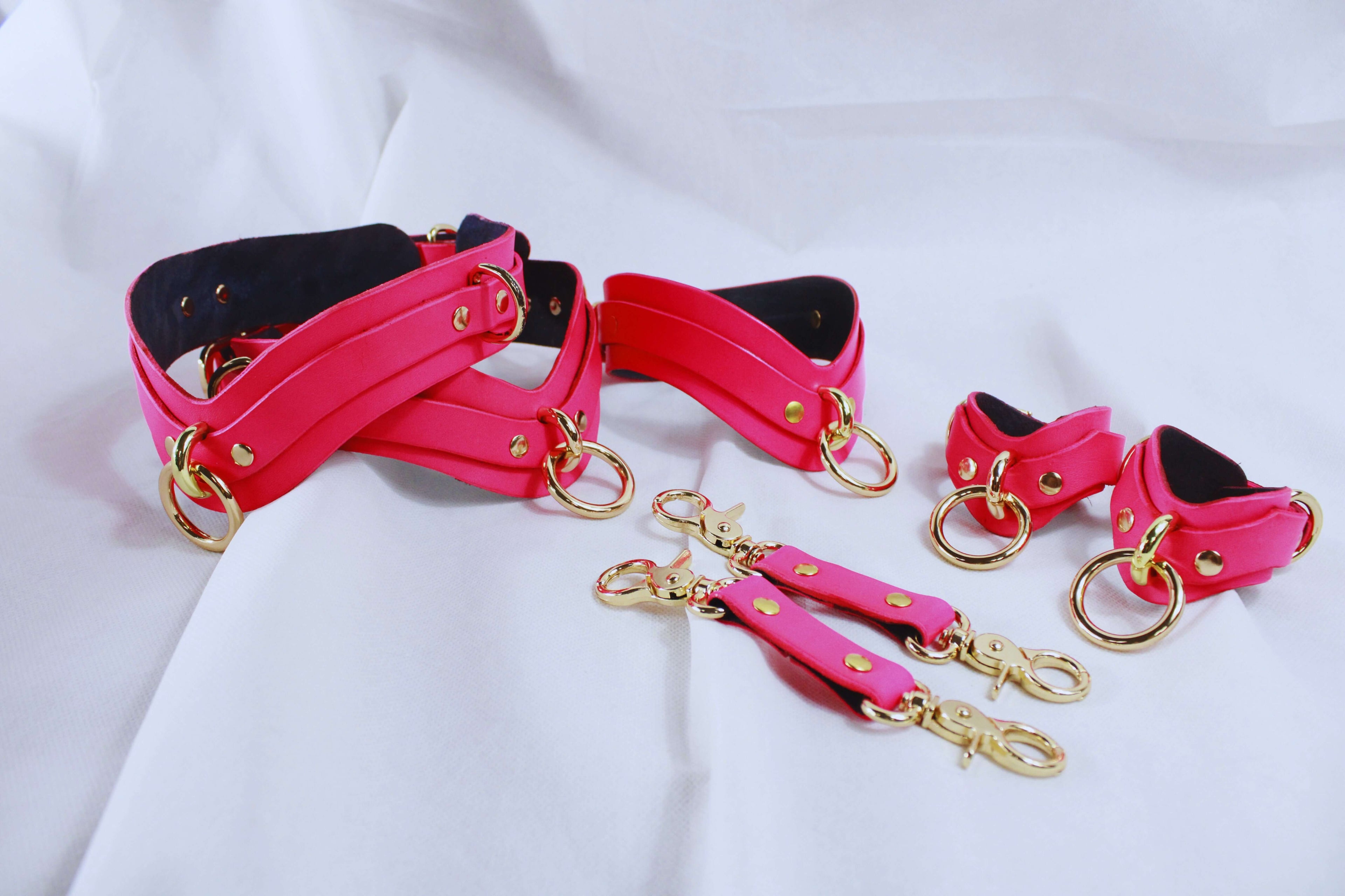 Bondage Gear pink restraint set with collar, cuffs, and connectors for BDSM play, featuring gold hardware and soft leather.