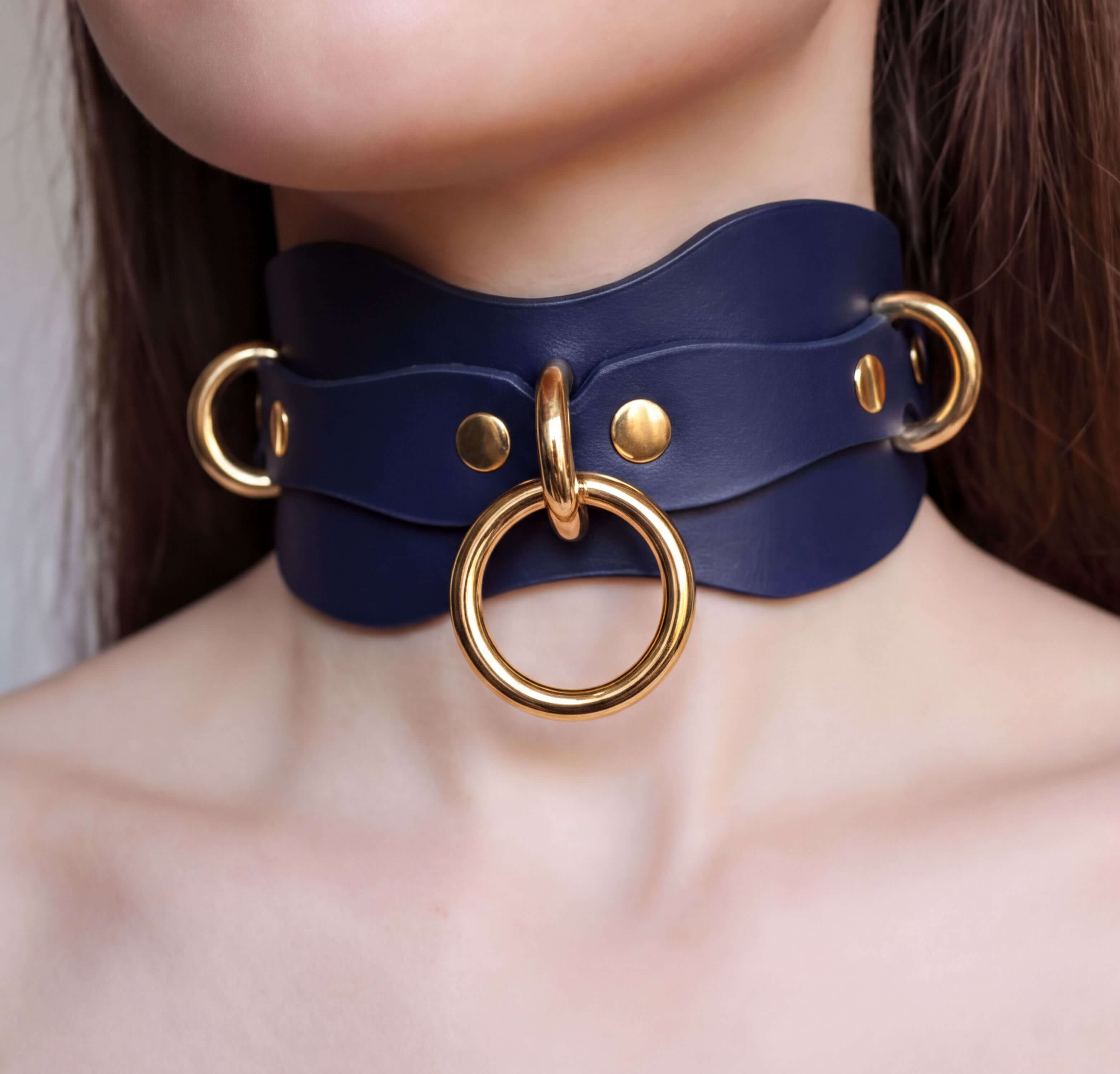 A close-up of a person's neck wearing a blue leather choker necklace with gold-colored metal rings.