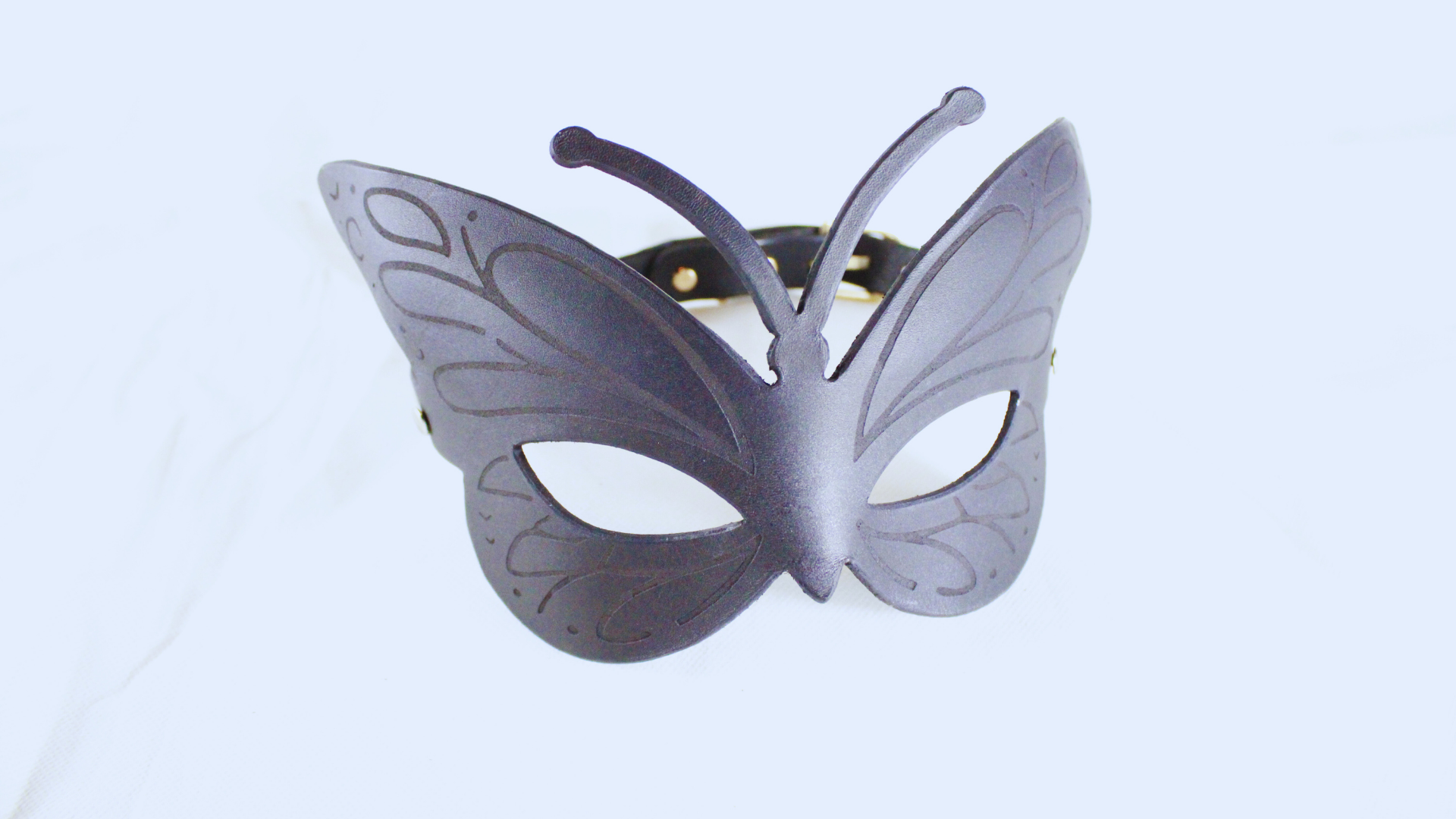 A black butterfly-shaped mask with intricate designs on its wings and a black strap.