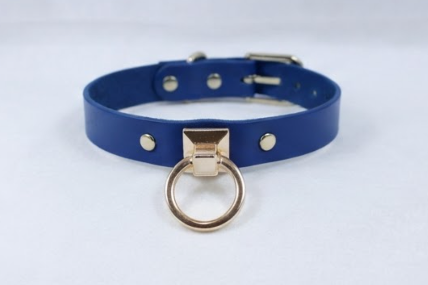 A blue leather choker necklace with a gold-colored metal ring and three small gold-colored studs on the collar.