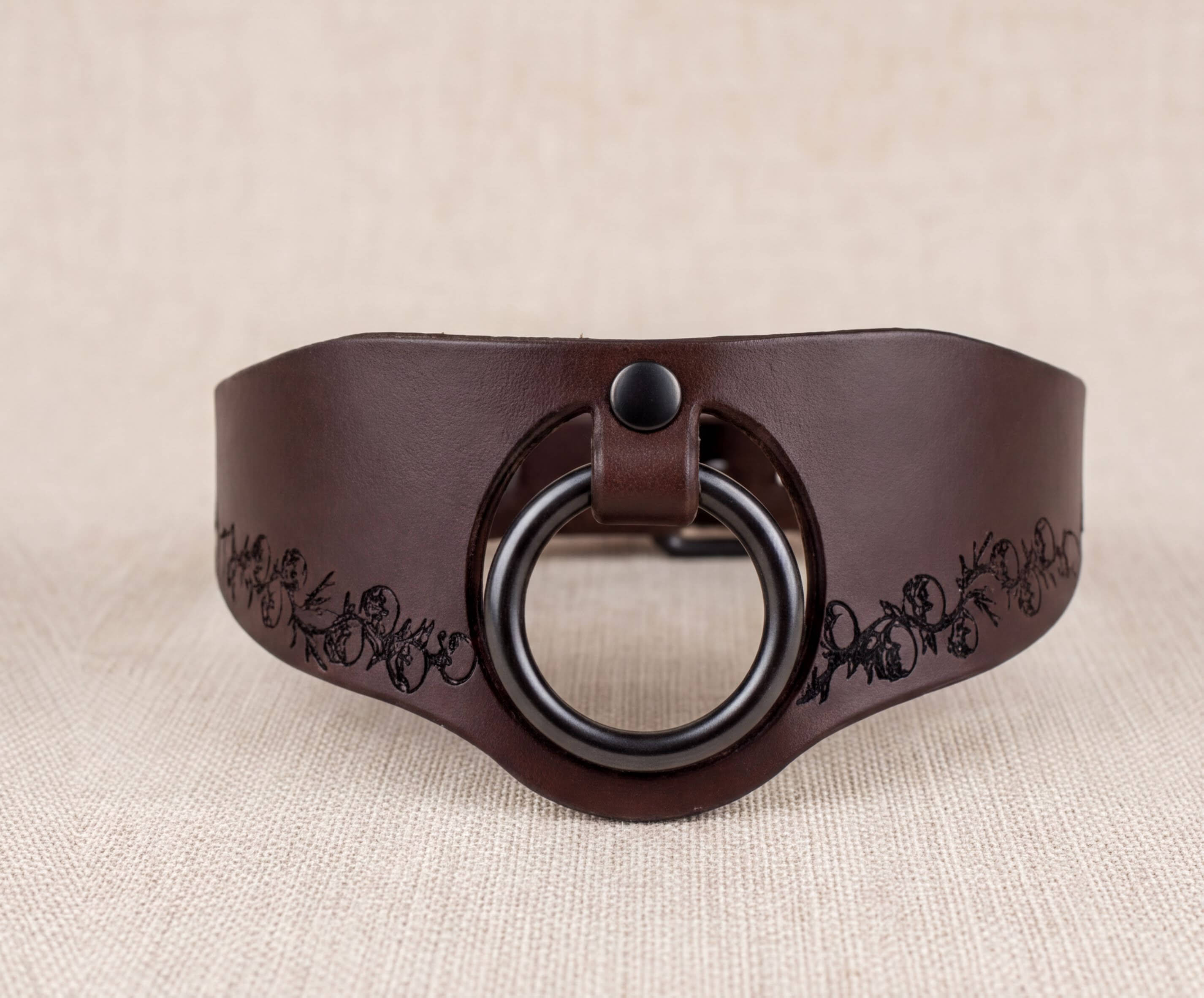 A brown leather collar with a black circular ring and a decorative pattern on the edge.
