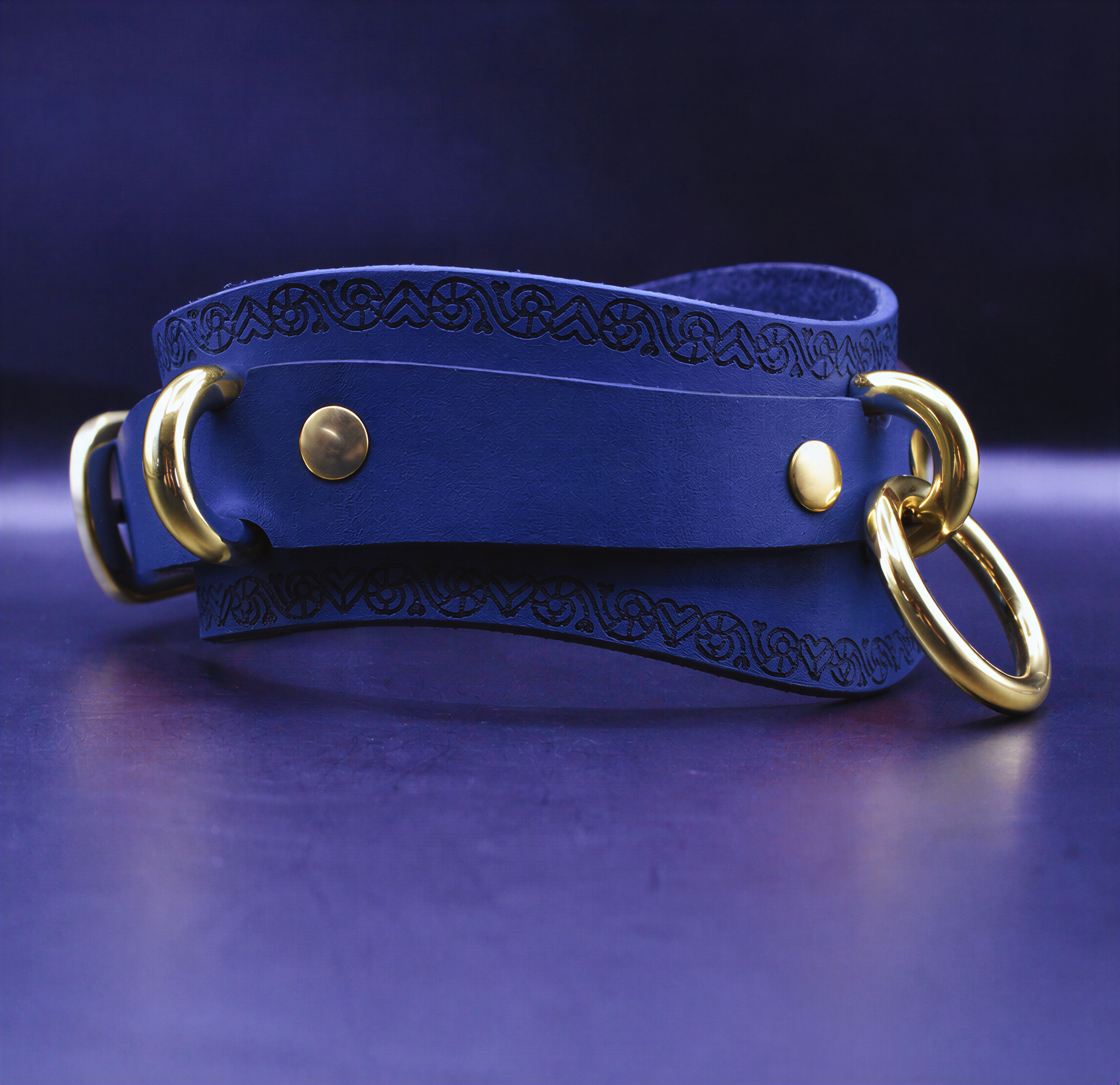 A blue leather choker necklace with gold-colored metal rings and a decorative pattern on the clasp.