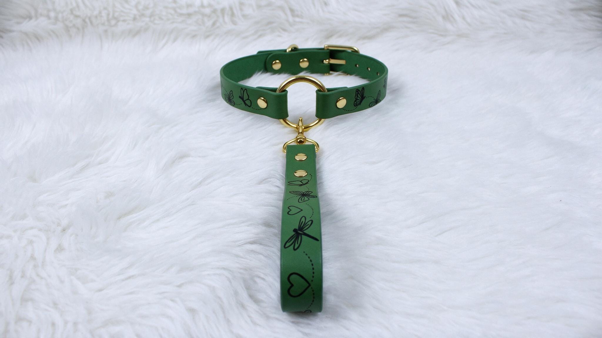 A green dog collar with a gold buckle and handle is displayed on a white furry surface.