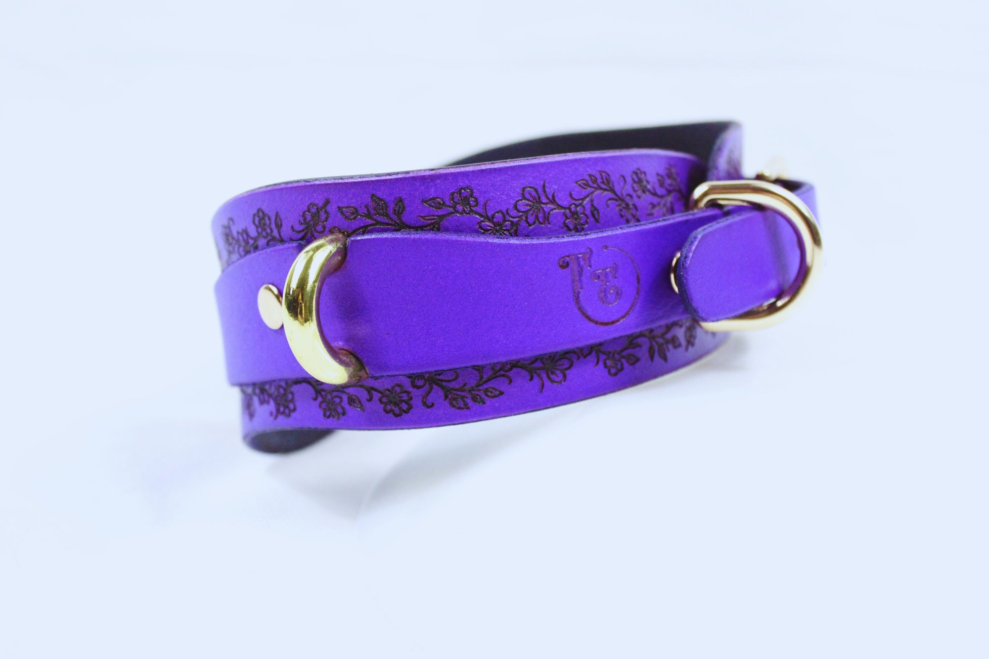 A purple leather strap with a floral pattern and two gold buckles.