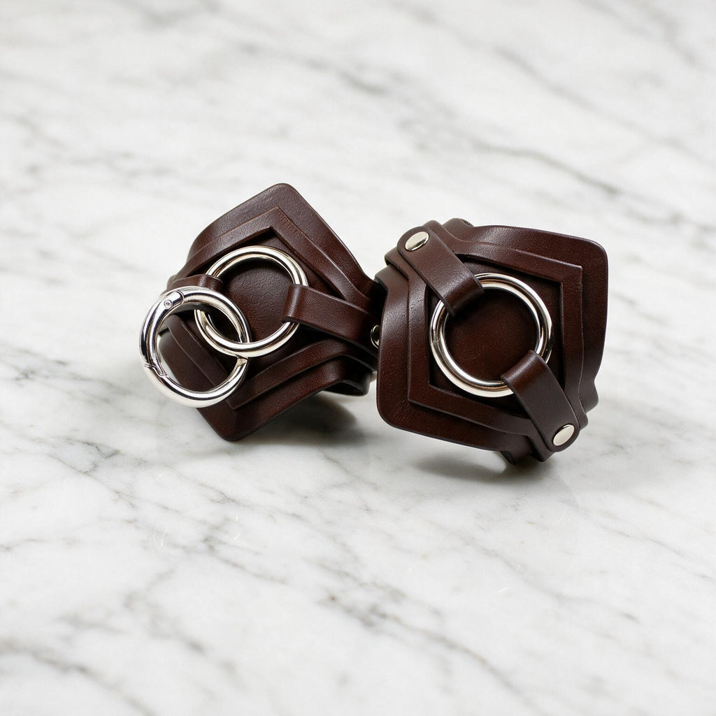 A pair of brown leather straps with metal rings, resting on a marble surface.