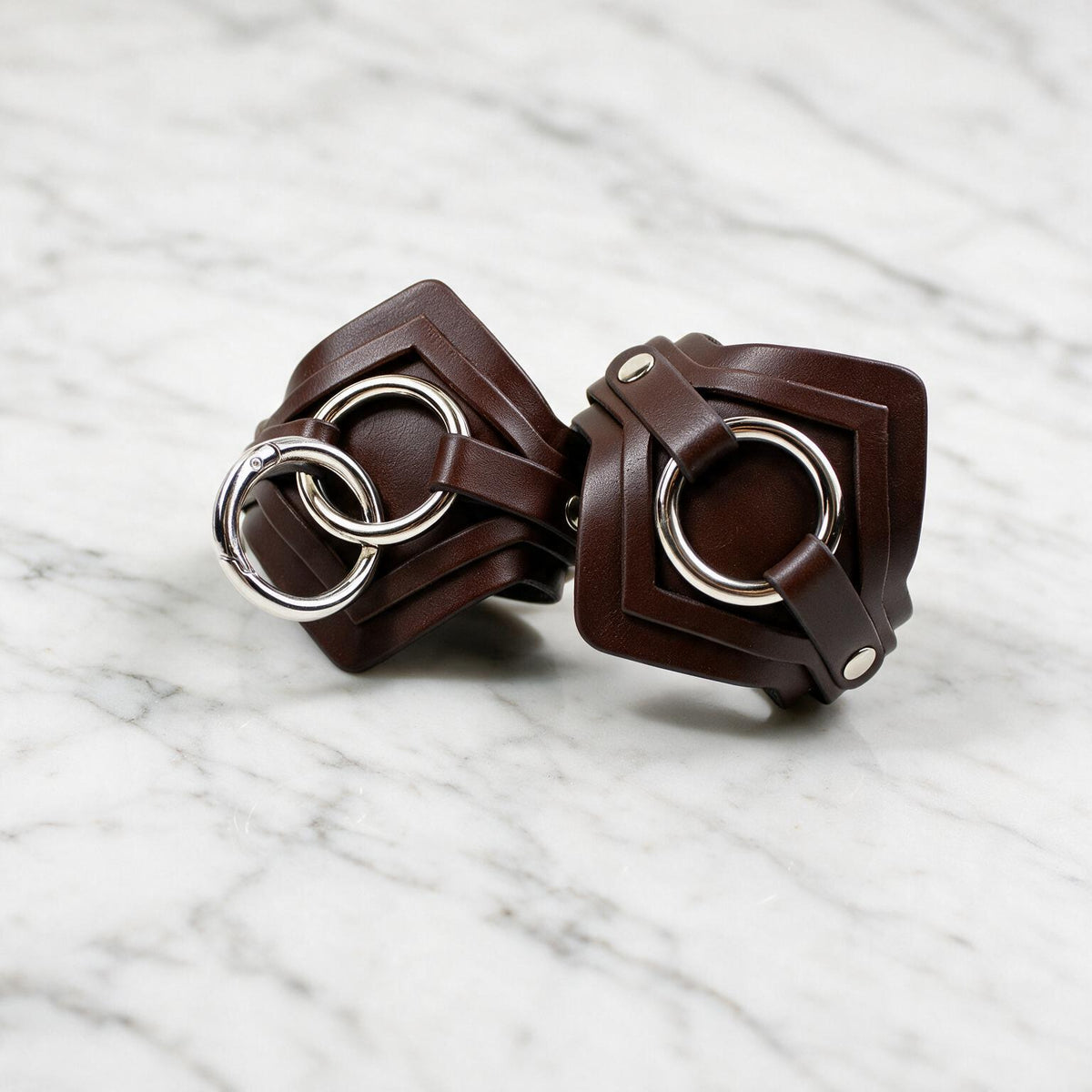 A pair of brown leather straps with metal rings, resting on a marble surface.