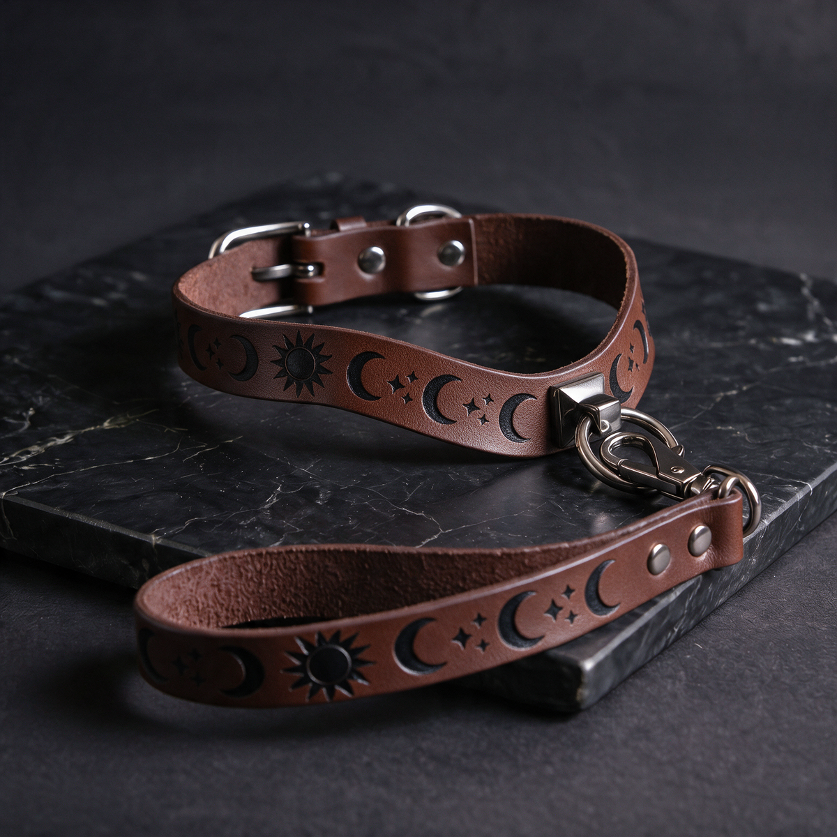 A brown leather collar with moon and star designs, and a matching leash attached to it, resting on a dark surface.
