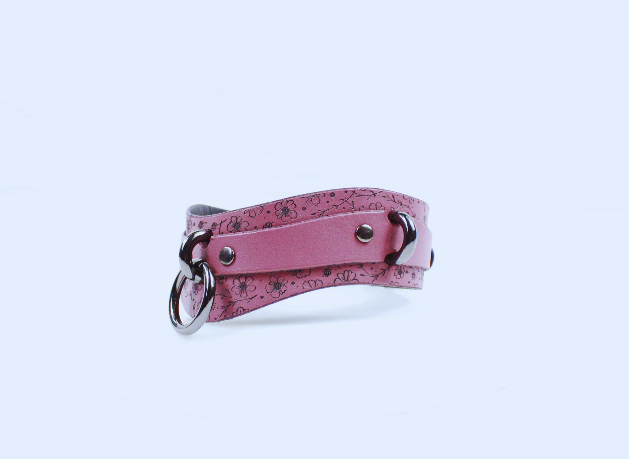 A pink leather choker necklace with a floral pattern and metal rings.