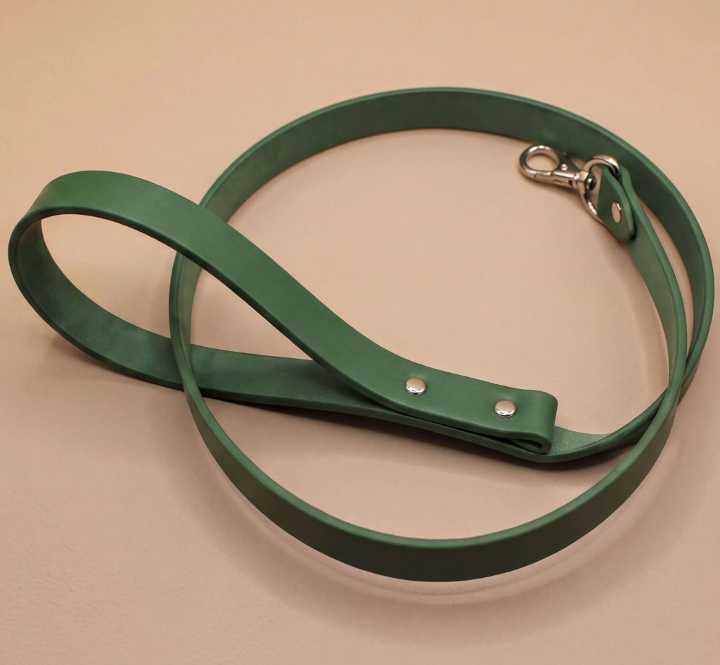 A green leather dog leash with a metal attachment is shown on a beige surface.