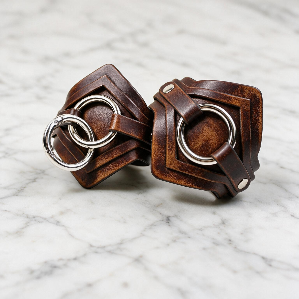 two leather straps with metal rings, placed on a marble surface.