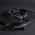 A black leather collar with a floral pattern and a matching leash are displayed on a dark surface.