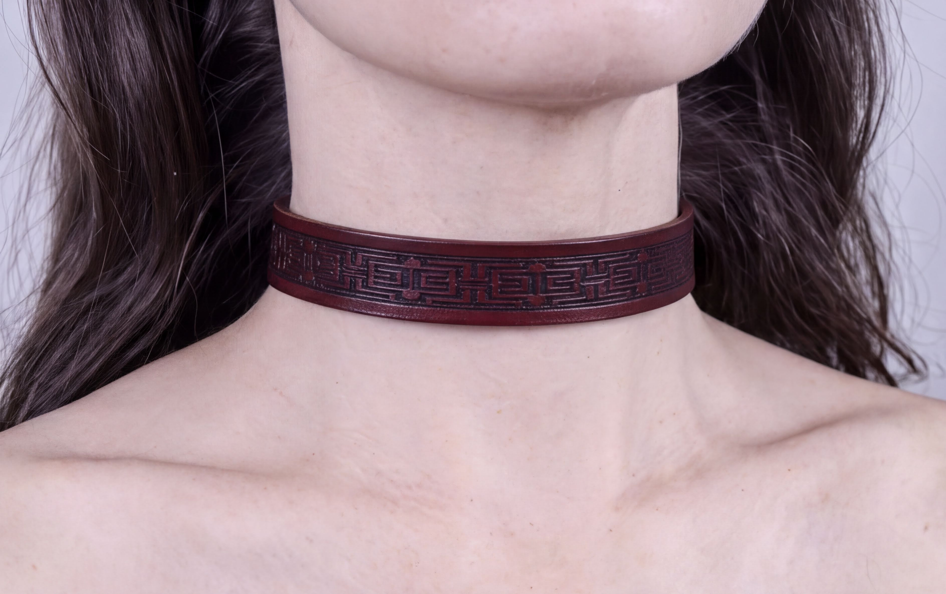 A close-up of a person's neck wearing a burgundy choker necklace with a geometric pattern.